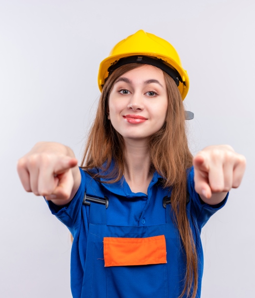 young woman builder worker in construction uniform and safety helmet looking confident smiling  pointing with index fingers to camera standing over white background